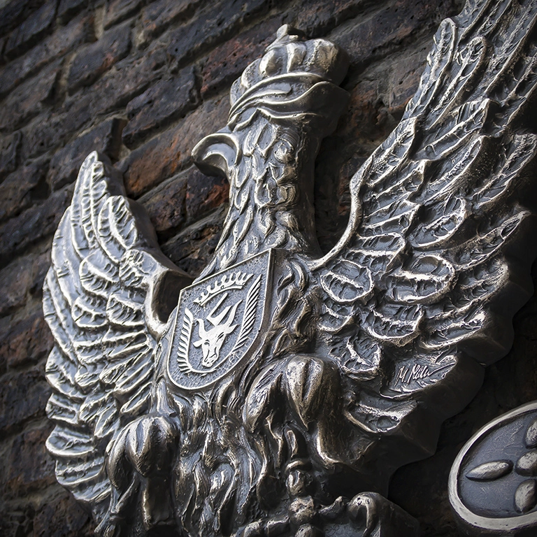 Tablica rzeźbiona - orzeł weteranów Detal tablicy pamiątkowej dla powstańców styczniowych – rzeźba orła z godłem Wiskitek na piersi i nazwiskami poległych u dołu.