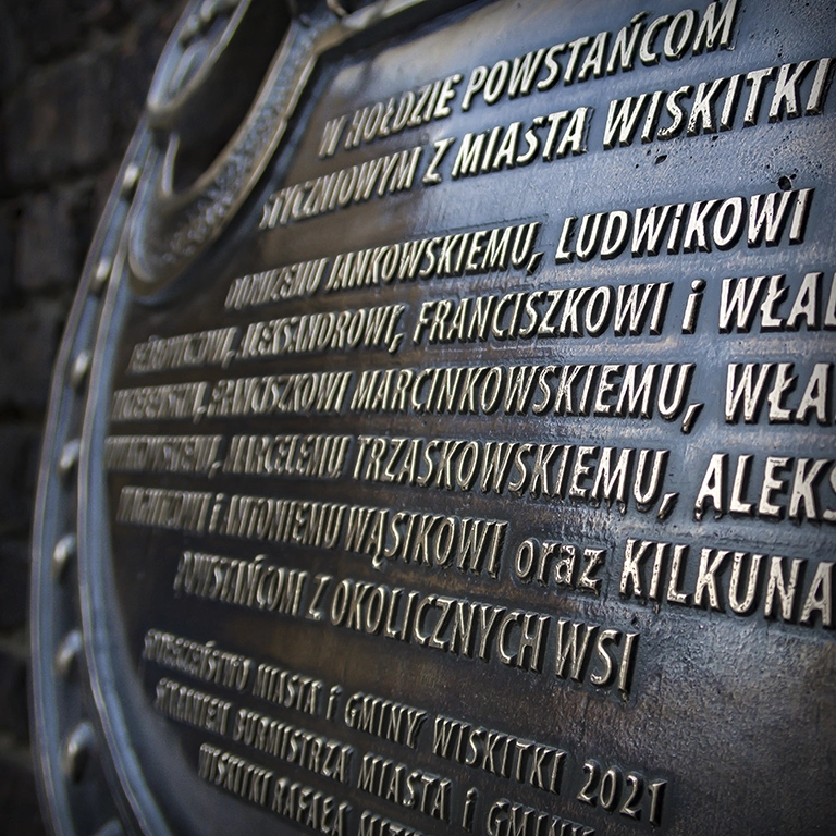 Tablica pamiątkowa, liternictwo Śląsk Upamiętnienie powstańców styczniowych z Wiskitek – tablica z rzeźbą inspirowaną orłem weteranów, z dodanym godłem miasta i nazwiskami bohaterów.