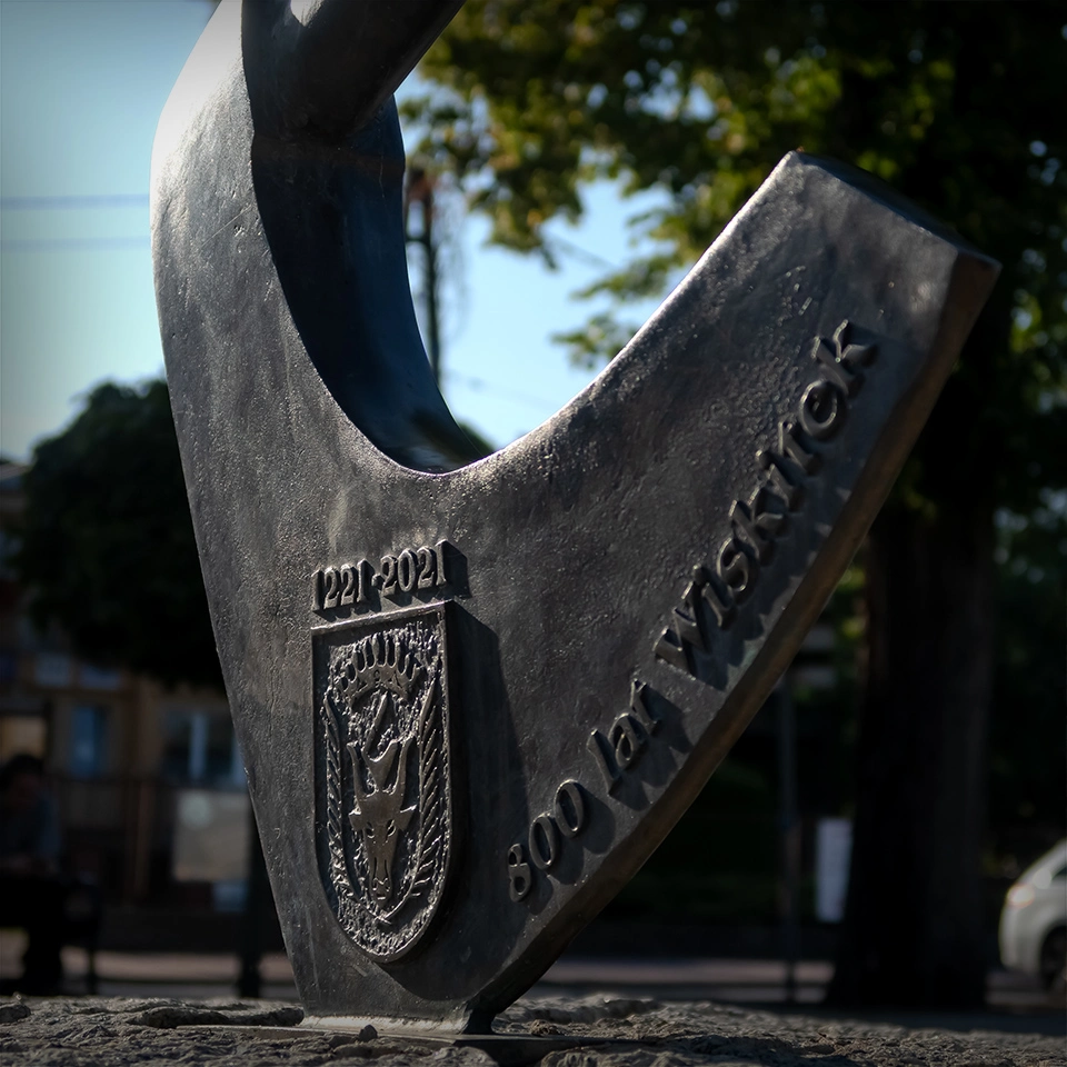 Rzeźba topora w Wiskitkach z herbem miasta, atrakcja turystów próbujących „wyrwać” narzędzie z ziemi.